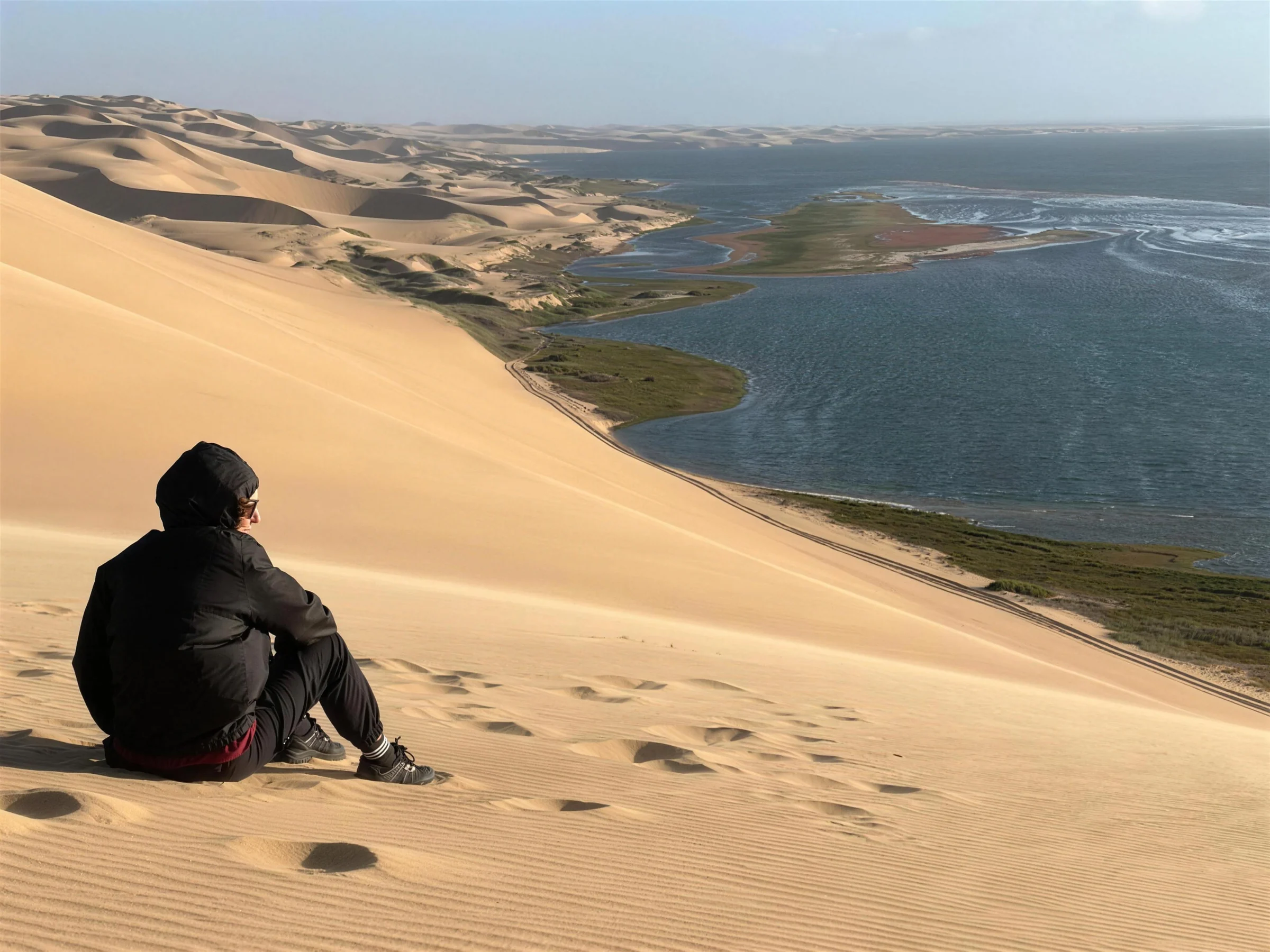 A person seated above dunes and water